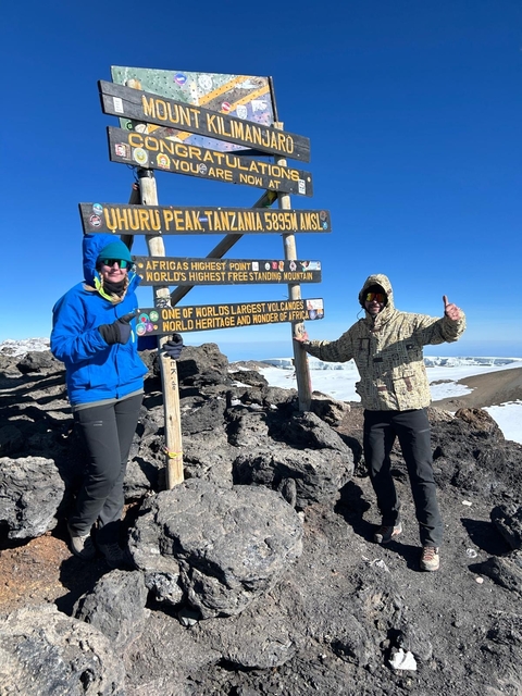 Two people posing at Uhuru Peak with signposts.