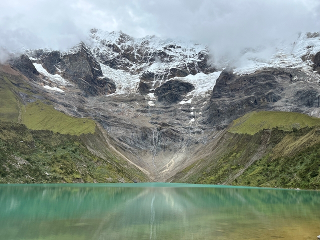 Turquoise lake surrounded by high snowy mountains and lush hills.