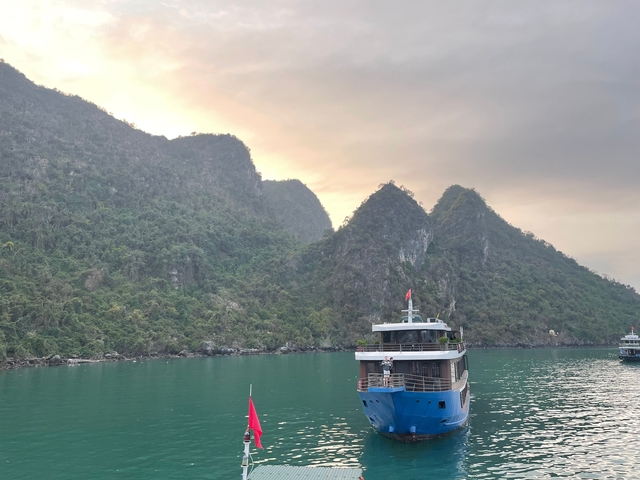 Boat on calm water with jagged cliffs and lush greenery in the background.