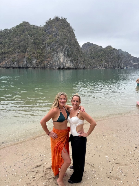 Two women smiling on a beach with cliffs in the background.