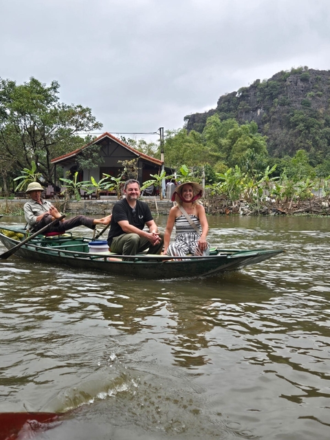 Two tourists on a boat rowed by a local man in a scenic waterway.