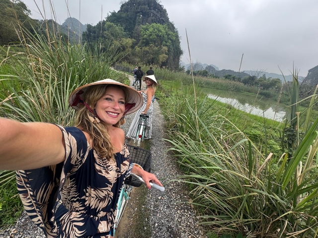 A woman taking a selfie while on a bicycle near water and plants.