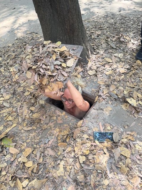 Person partially inside a narrow tunnel camouflaged with leaves.