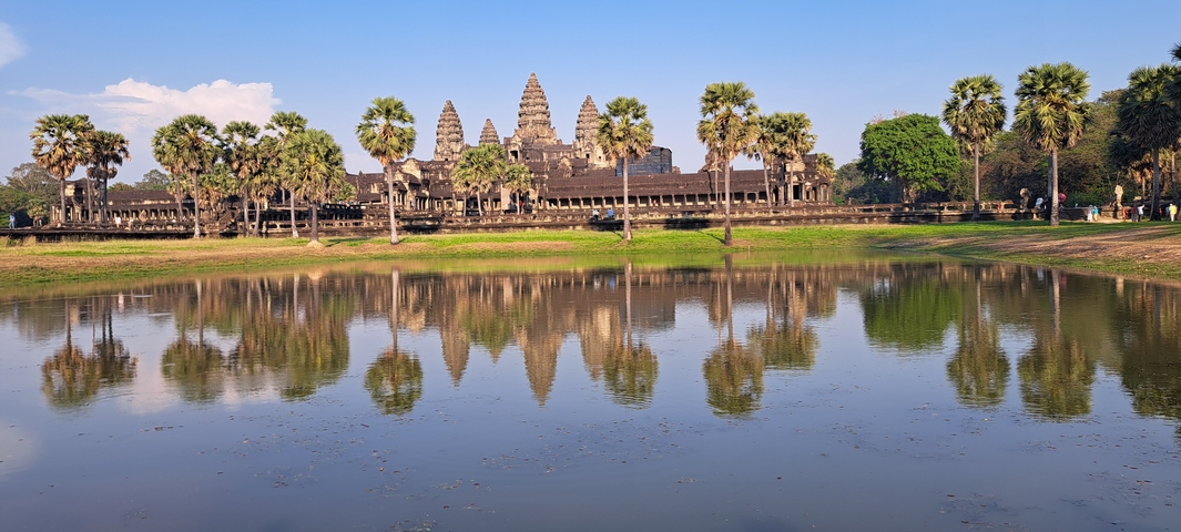 Iconic Angkor Wat temple reflected in a pond with palm trees.