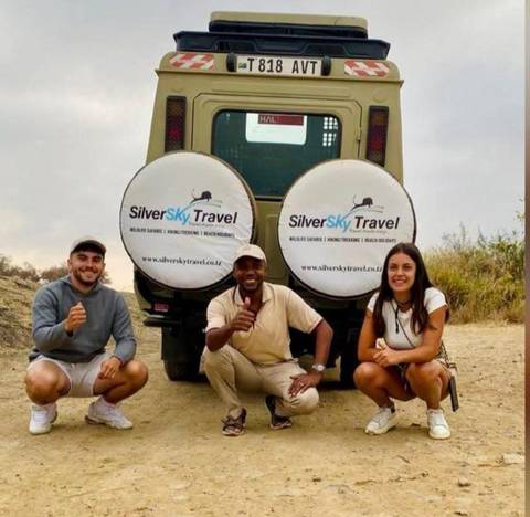 Three people posing in front of a safari vehicle with travel logos.