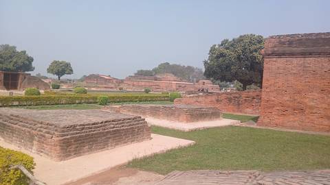 Ancient brick platforms and walls surrounded by grass and trees.