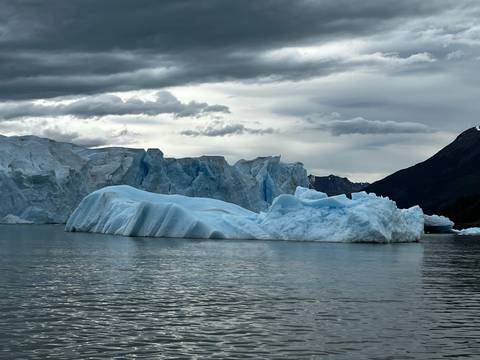 Large iceberg floating in calm waters under a cloudy sky.