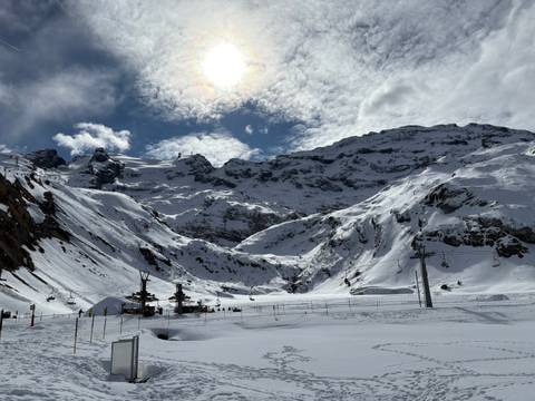 Mountainous snowy landscape with ski lifts, under a bright sun.