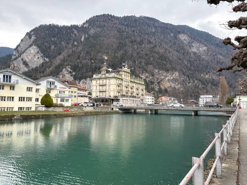 Quaint European town by a river with a mountainous backdrop.