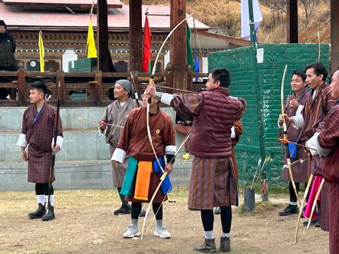 Group of men in traditional Bhutanese attire practicing archery.