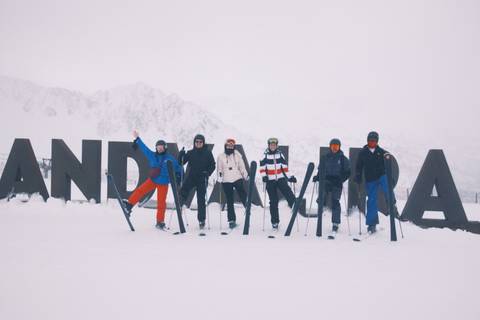 Skiers posing in front of a large sign in snowy conditions.