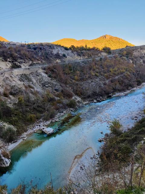 A clear river running through rocky terrain with bushes along the sides.