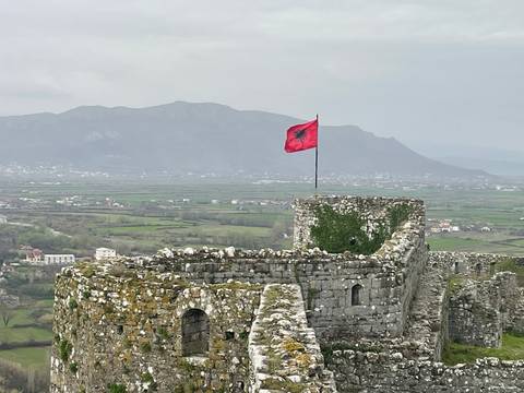 Ancient fortress with an Albanian flag and mountains in the background.