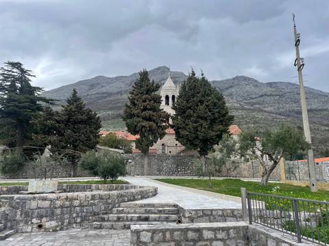 Stately building with church and trees in front with mountains behind.