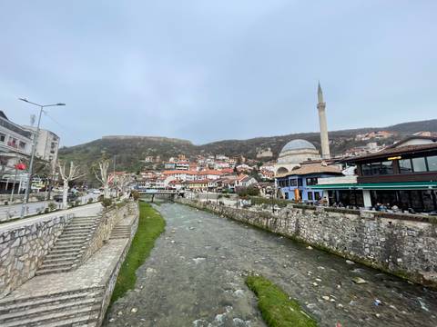 Scenic view of a river running through a town with a mosque and hills in the background.