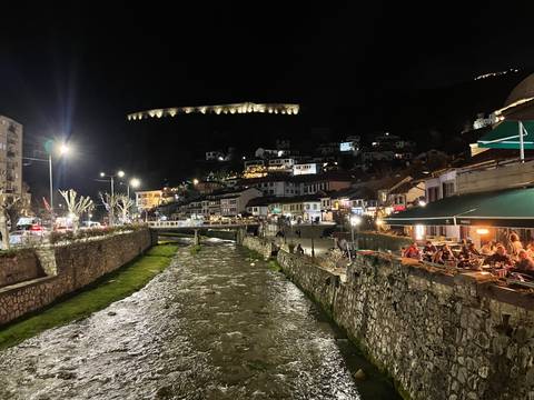 Night view of a town with a river, illuminated buildings, and a fortress on a hill.