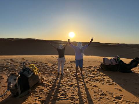 Two people admiring a sunset over the desert with camels nearby.