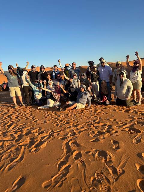 Group of people posing in the desert with sand dunes.