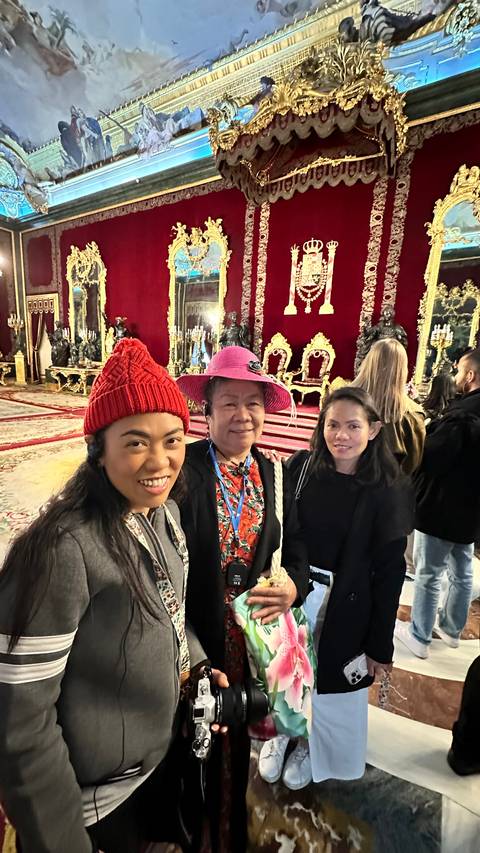 Three people posing inside a lavishly decorated room with red walls.