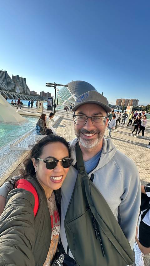 Couple posing in front of futuristic buildings and water feature.