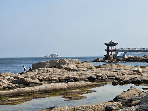 A rocky shoreline with a traditional pavilion and distant island in the sea.