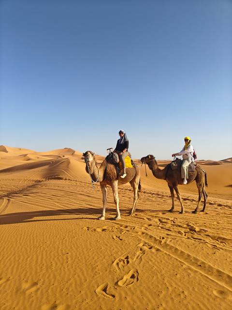 Two people riding camels in the desert dunes.