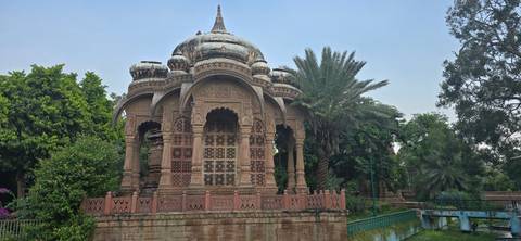 A beautifully carved pavilion in a garden setting.