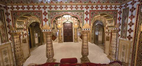 An ornately decorated, mirror-covered room with arches and pillars.