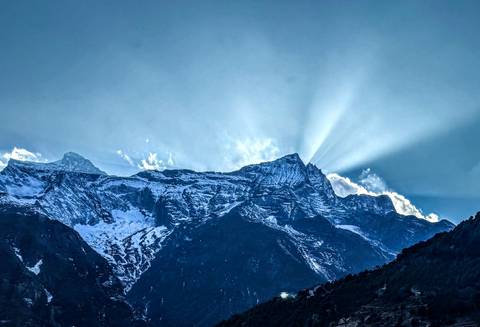 Sun rays shining over snow-capped mountains with clear sky.