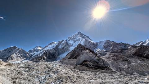 Sun-lit mountain range with prominent peak under a bright sky.