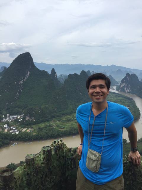 A smiling man with scenic karst mountains in the background.