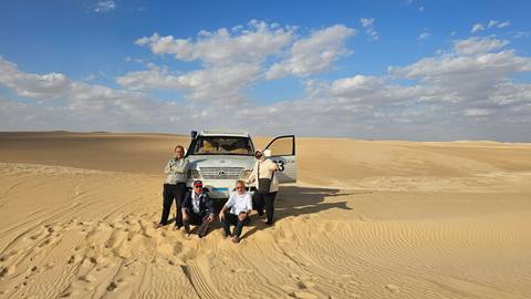 Group of people posing in a desert landscape with a vehicle.