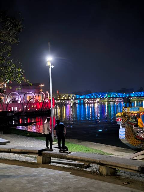 Night view of a bridge and building illuminated with colorful lights reflecting on the water.