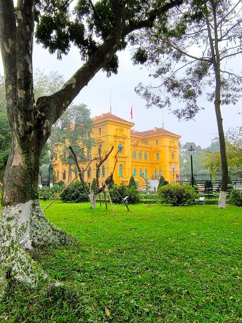 Yellow colonial building surrounded by lush green trees and grass.