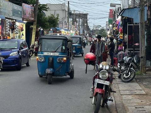 Street scene with tuk-tuks and motorbikes on a busy lane.