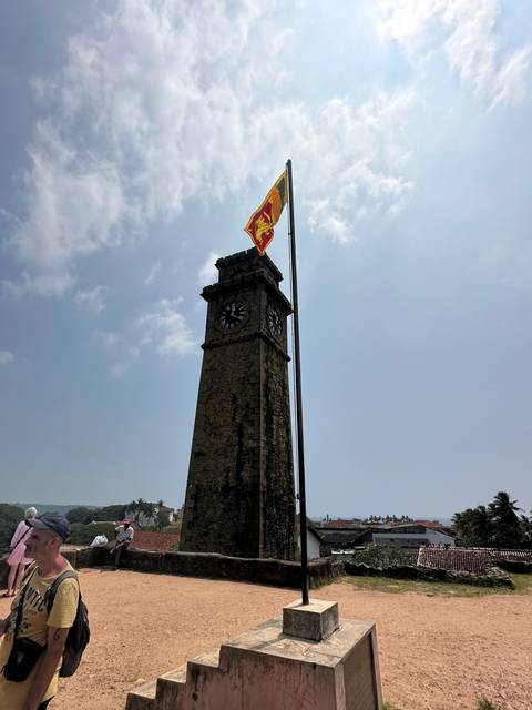 Clock tower with a flag at the top against a bright sky.