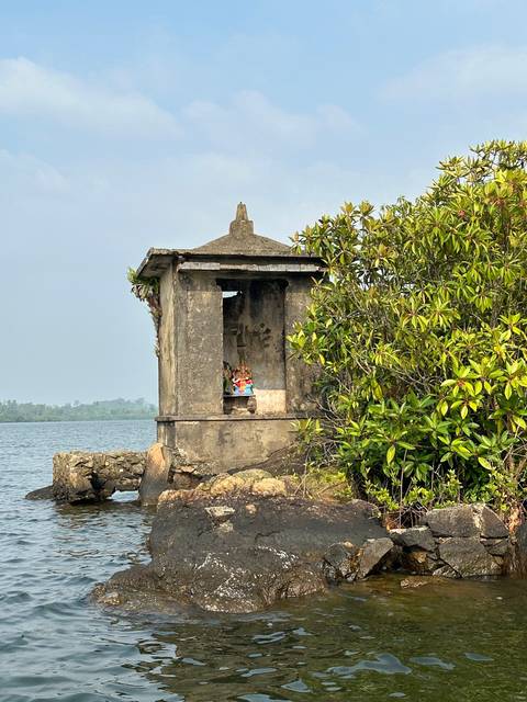 Stone structure beside a body of water, partially obscured by foliage.