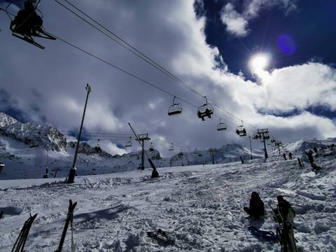 Ski lift ascending a snowy mountain under a partially cloudy sky.
