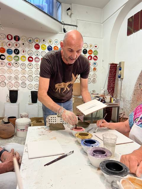 A man demonstrating pottery painting in an art studio.