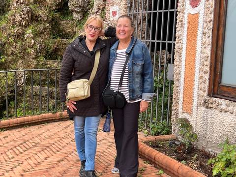 Two women standing on a brick terrace outdoors.