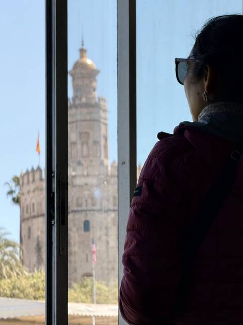 Person standing by a window with view of a historic tower.