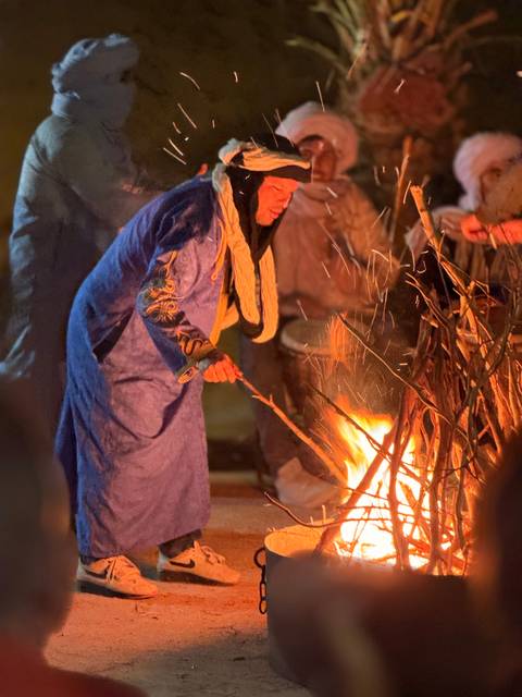 Person in traditional attire tending to a fire at night.