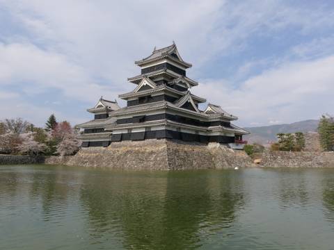Traditional Japanese castle surrounded by a moat and cherry blossoms.
