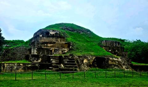 Pyramid-shaped ancient structure in green landscape.