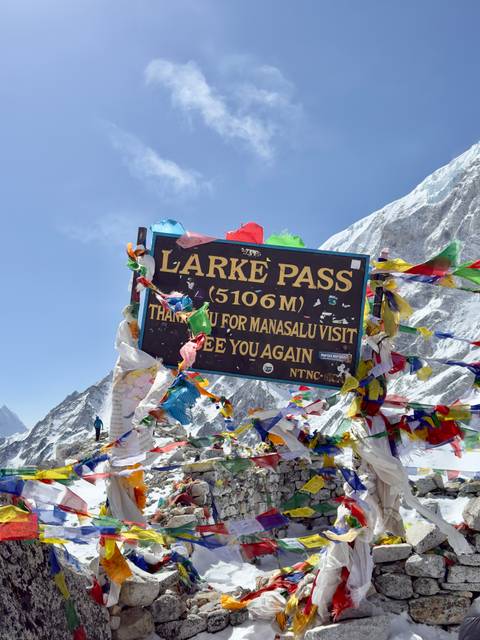 Sign at Larke Pass with colorful flags against mountain backdrop.