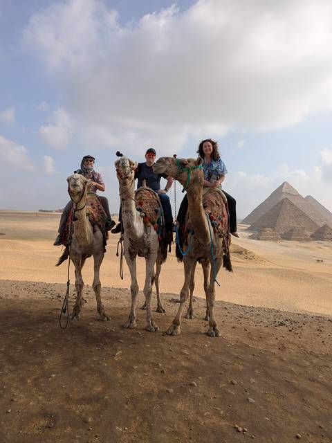 Group of people riding camels in front of pyramids.
