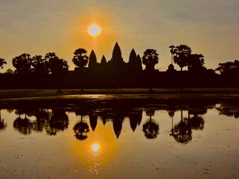 Silhouette of Angkor Wat with reflection on the water during sunset.