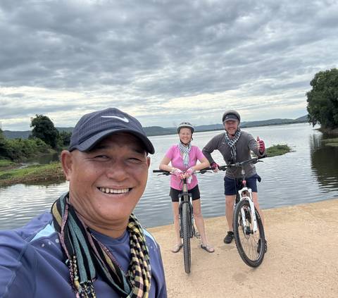 Cyclists taking a selfie with a lake and cloudy sky in the background.