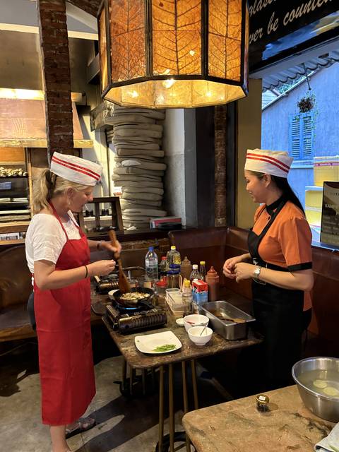 Two women cooking in a kitchen, wearing aprons and hats.