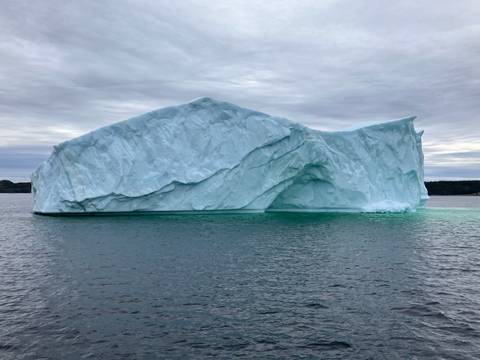 A large iceberg floating in the ocean under a cloudy sky.